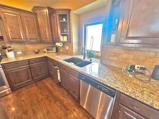 kitchen featuring backsplash, light stone countertops, dark wood finished floors, stainless steel dishwasher, and a sink