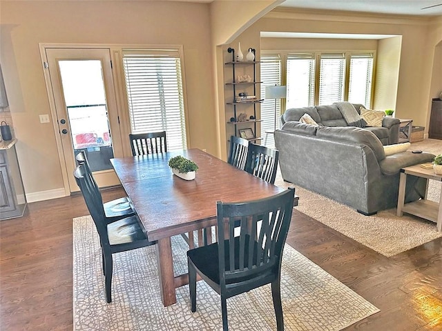 dining space featuring baseboards, arched walkways, dark wood finished floors, and ornamental molding