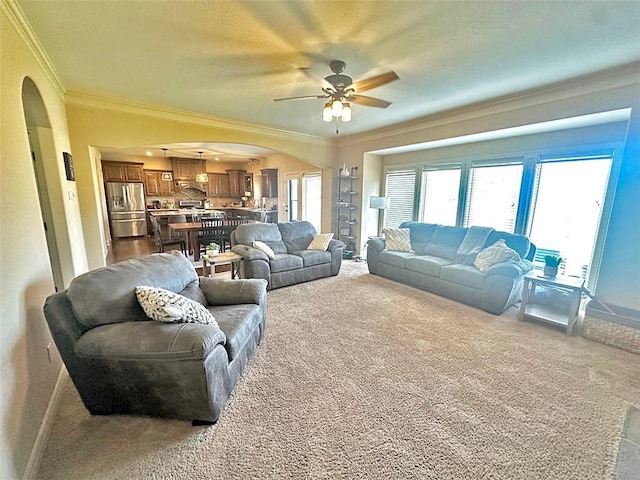 carpeted living area featuring ceiling fan, baseboards, arched walkways, and ornamental molding