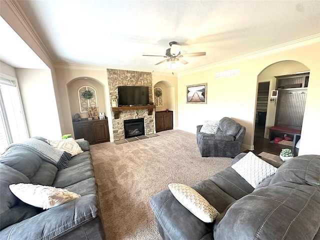 living area featuring ceiling fan, carpet floors, a stone fireplace, and ornamental molding