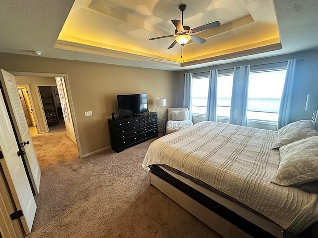 carpeted bedroom with a tray ceiling, baseboards, and ceiling fan