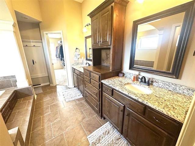 full bathroom with stone tile flooring, two vanities, a bathtub, and a sink