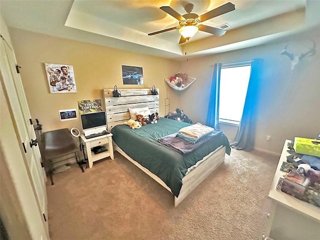 carpeted bedroom with a raised ceiling, visible vents, and ceiling fan