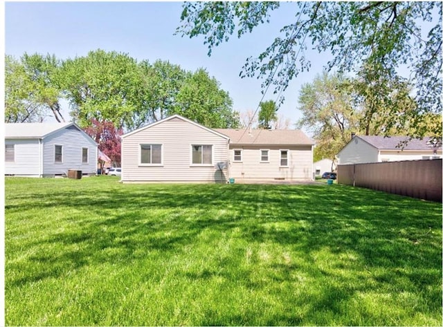 rear view of property featuring a lawn and fence