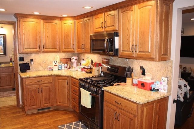 kitchen featuring stainless steel microwave, black gas range, light stone countertops, and light wood-style flooring