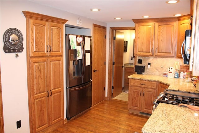 kitchen with backsplash, light stone counters, light wood finished floors, and stainless steel appliances