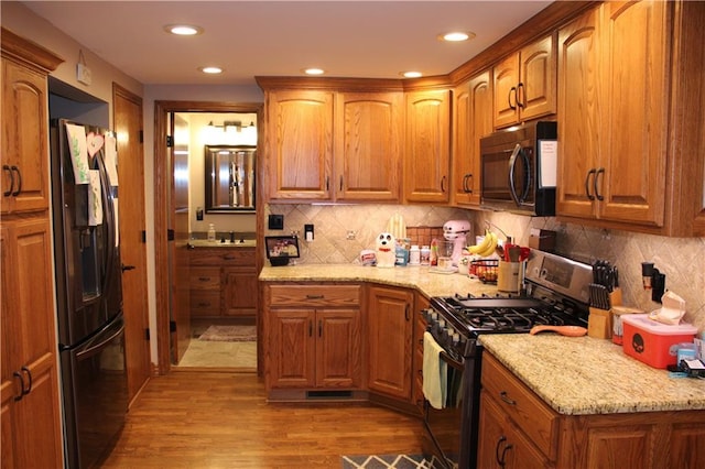 kitchen featuring light stone counters, brown cabinets, black appliances, and wood finished floors