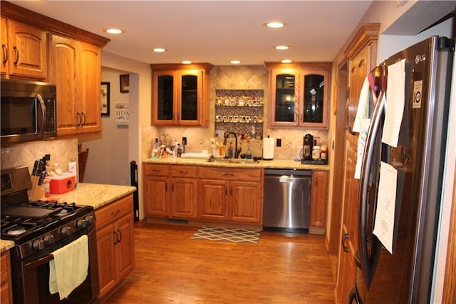 kitchen with light stone countertops, appliances with stainless steel finishes, wood finished floors, and a sink