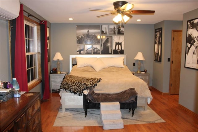 bedroom featuring recessed lighting, wood finished floors, baseboards, and a wall mounted air conditioner