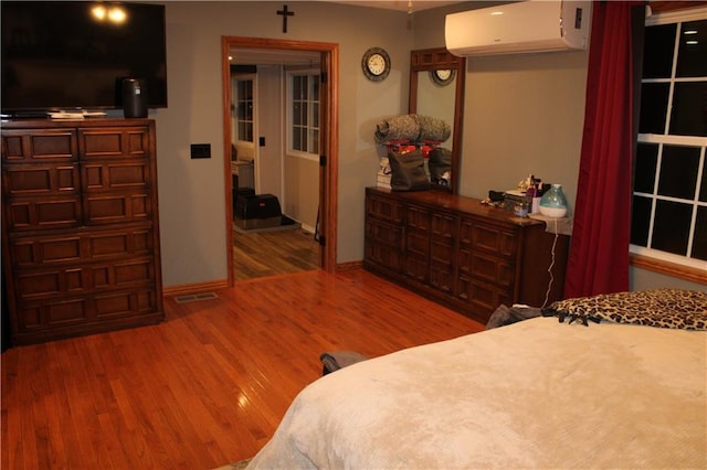 bedroom with an AC wall unit, baseboards, and wood finished floors