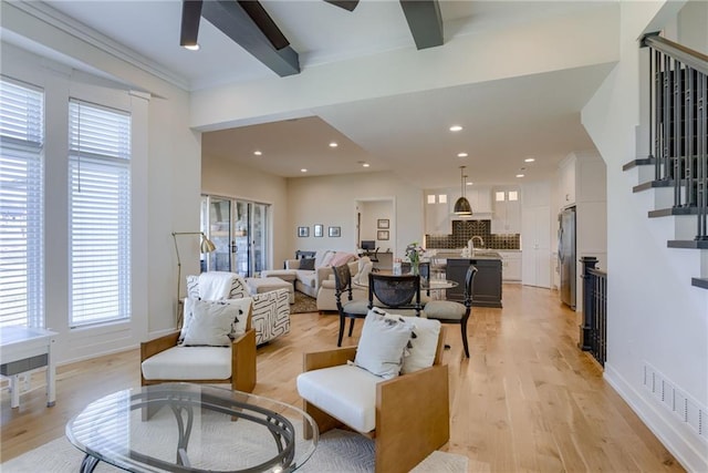 living area with visible vents, stairway, beamed ceiling, light wood-style floors, and a ceiling fan