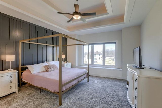 bedroom with a tray ceiling, light carpet, baseboards, and ceiling fan