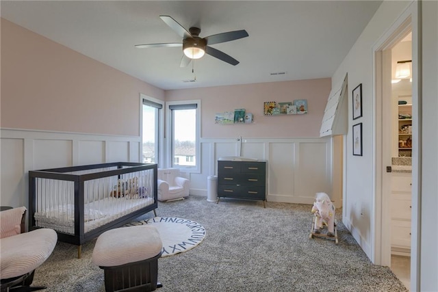 bedroom with visible vents, ceiling fan, a wainscoted wall, light colored carpet, and a decorative wall