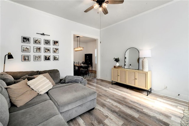 living area with light wood-style flooring, a ceiling fan, baseboards, and ornamental molding