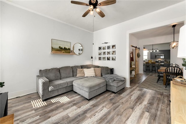 living area with crown molding, wood finished floors, baseboards, and ceiling fan