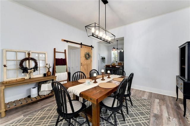 dining area with wood finished floors, baseboards, crown molding, a barn door, and a notable chandelier