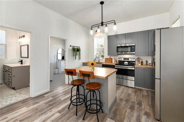 kitchen featuring a breakfast bar area, appliances with stainless steel finishes, butcher block counters, and gray cabinetry