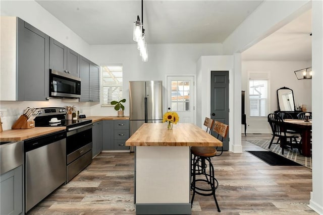 kitchen featuring a breakfast bar area, gray cabinetry, wooden counters, and stainless steel appliances