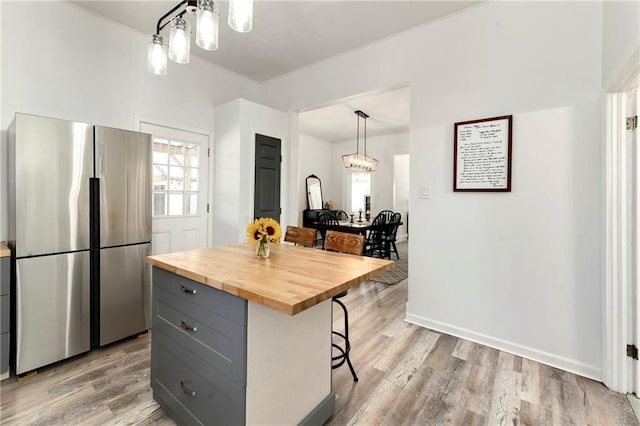 kitchen featuring a kitchen bar, gray cabinets, freestanding refrigerator, butcher block counters, and a chandelier