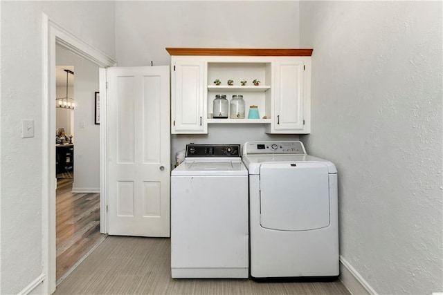 clothes washing area featuring baseboards, light wood finished floors, a textured wall, cabinet space, and washing machine and dryer