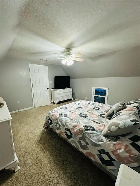 bedroom featuring lofted ceiling, a textured ceiling, a ceiling fan, and light carpet