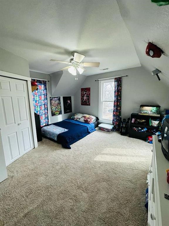 bedroom featuring carpet flooring, a textured ceiling, visible vents, lofted ceiling, and a ceiling fan