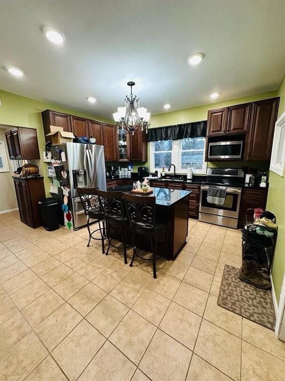 kitchen with a kitchen breakfast bar, dark countertops, light tile patterned floors, appliances with stainless steel finishes, and a notable chandelier