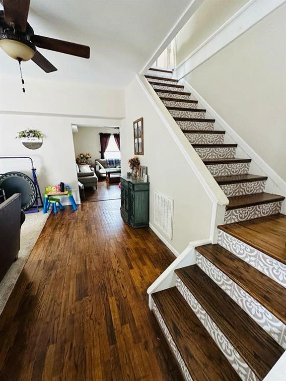 stairs with a ceiling fan, visible vents, and hardwood / wood-style flooring