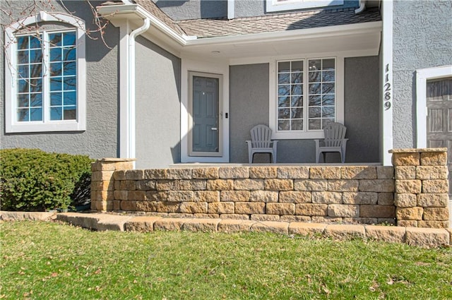 property entrance with stucco siding, covered porch, and a shingled roof