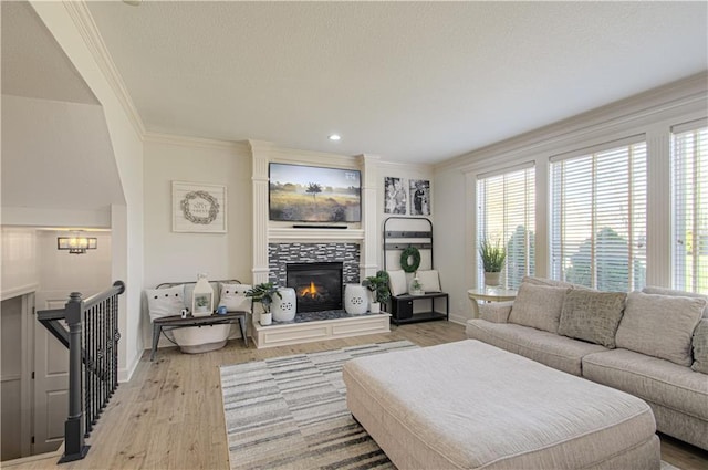 living room featuring a tile fireplace, light wood-type flooring, crown molding, and baseboards