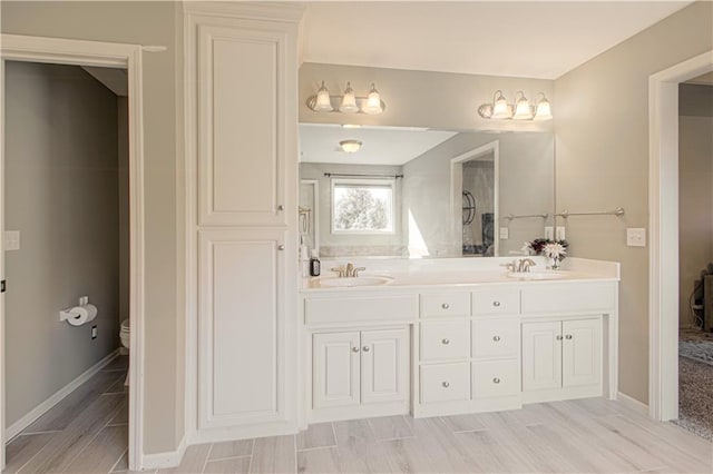 bathroom featuring baseboards, wood finish floors, toilet, double vanity, and a sink