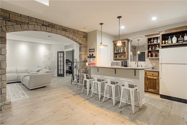 kitchen with a kitchen bar, light wood-style flooring, freestanding refrigerator, arched walkways, and open shelves