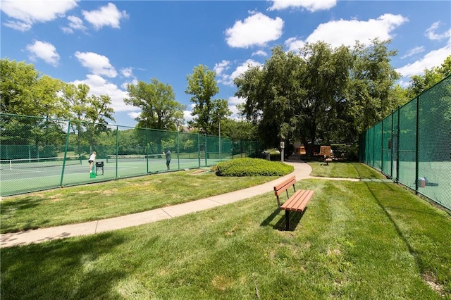 view of tennis court with a lawn and fence