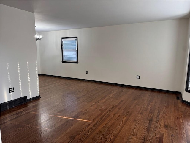 unfurnished room featuring baseboards, an inviting chandelier, and wood finished floors