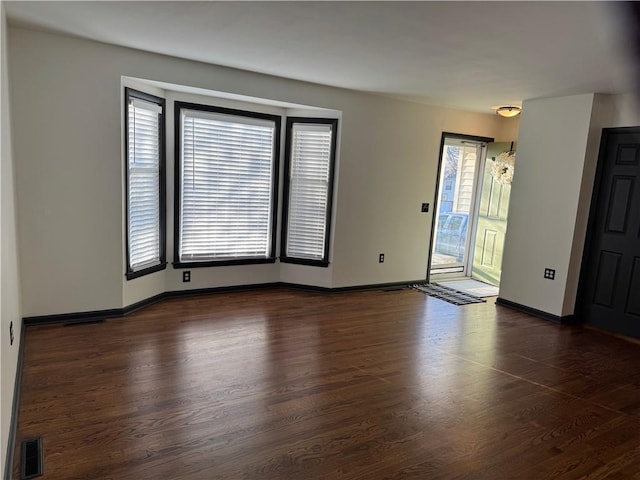 spare room featuring visible vents, dark wood-style flooring, and baseboards