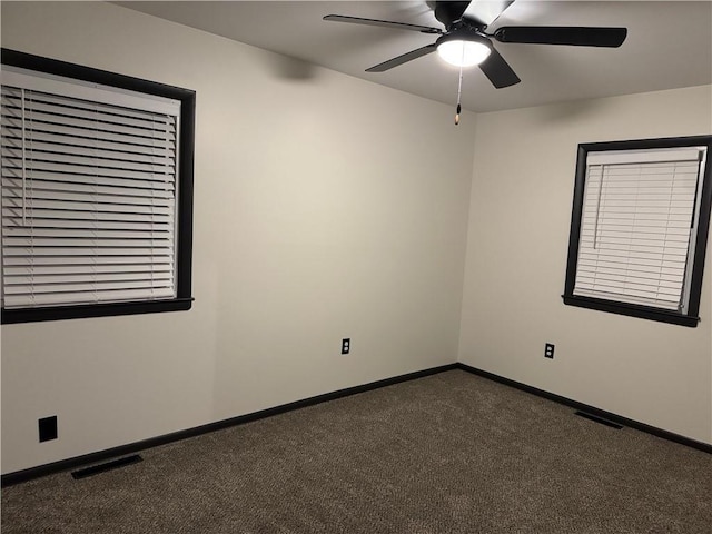 spare room featuring visible vents, baseboards, dark colored carpet, and ceiling fan