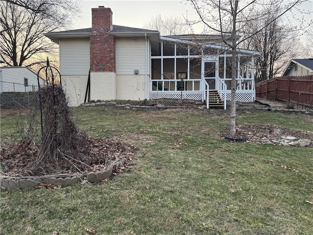 rear view of house featuring a lawn, a chimney, fence, and a sunroom