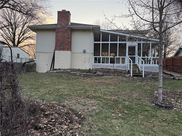 back of property featuring a lawn, fence, a sunroom, and a chimney