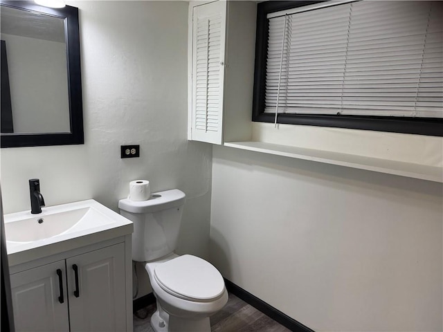 half bathroom featuring vanity, toilet, wood finished floors, and baseboards