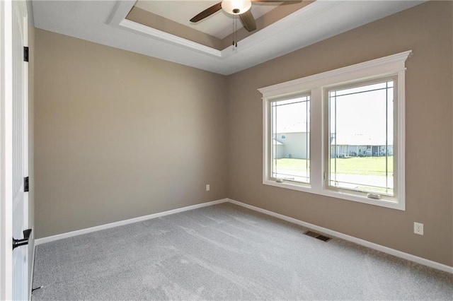 spare room featuring baseboards, visible vents, carpet floors, a tray ceiling, and ceiling fan