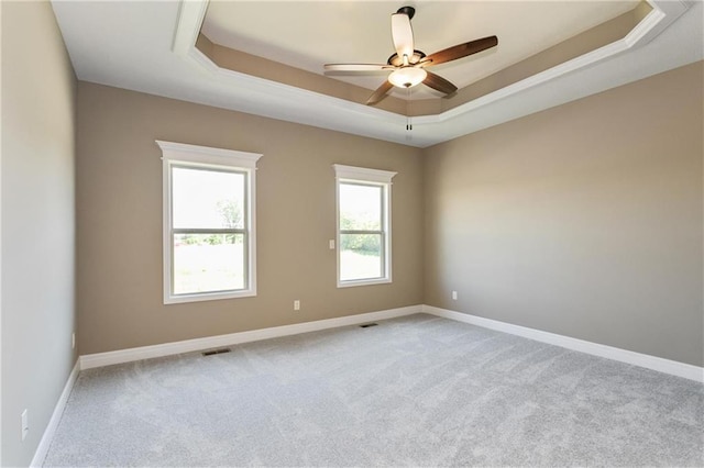 empty room featuring a tray ceiling, baseboards, carpet, and visible vents