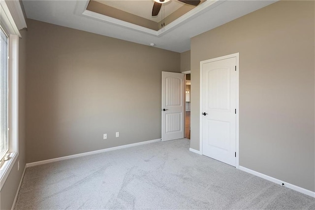 carpeted empty room featuring baseboards, a raised ceiling, and ceiling fan