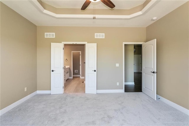 unfurnished bedroom with a raised ceiling, light colored carpet, and visible vents