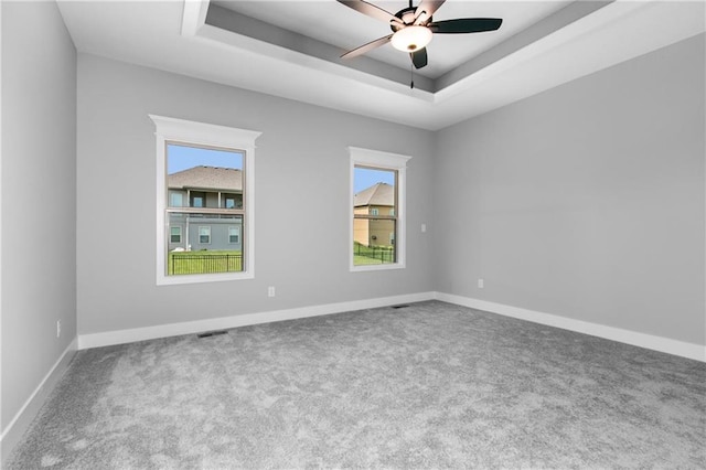 unfurnished room featuring a tray ceiling, baseboards, carpet floors, and a ceiling fan