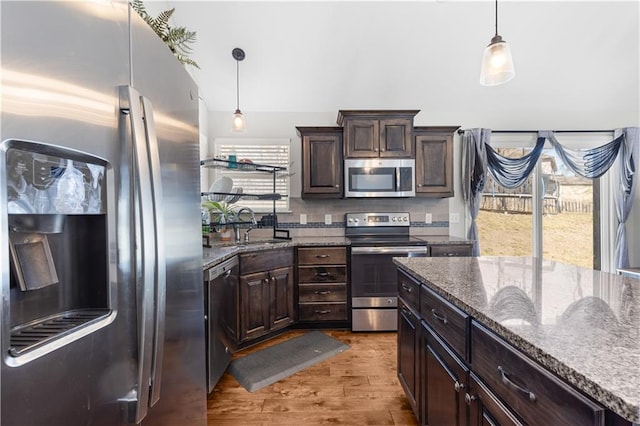 kitchen with wood finished floors, a sink, stainless steel appliances, dark brown cabinets, and decorative light fixtures