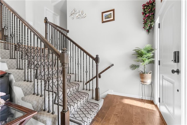 staircase featuring a high ceiling, baseboards, and wood finished floors