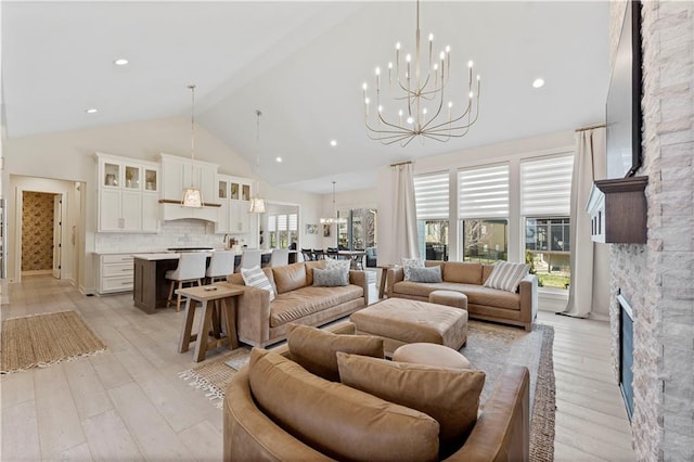 living area featuring an inviting chandelier, a fireplace, light wood-type flooring, and high vaulted ceiling