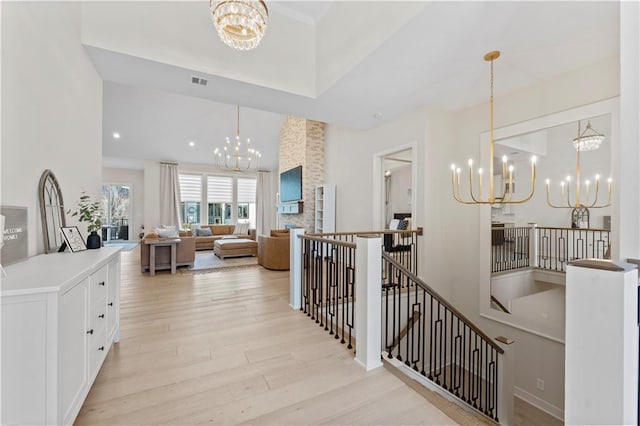 corridor featuring visible vents, light wood-type flooring, an upstairs landing, a high ceiling, and a notable chandelier