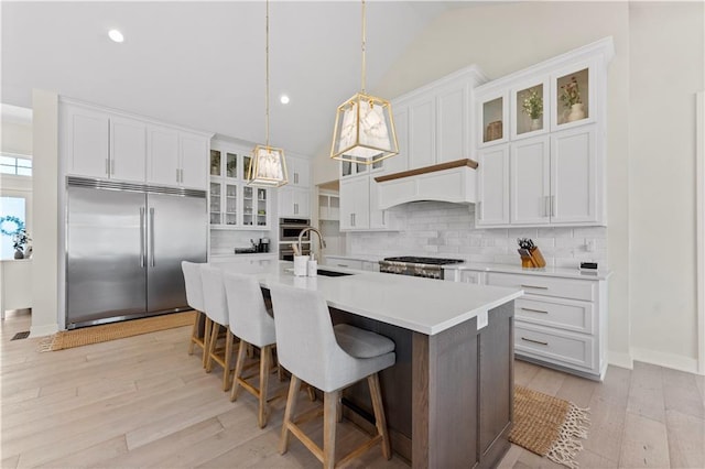 kitchen featuring tasteful backsplash, light wood-type flooring, appliances with stainless steel finishes, custom exhaust hood, and a sink