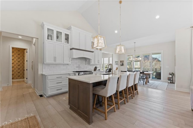 kitchen with a kitchen island with sink, a sink, stove, light countertops, and light wood-type flooring